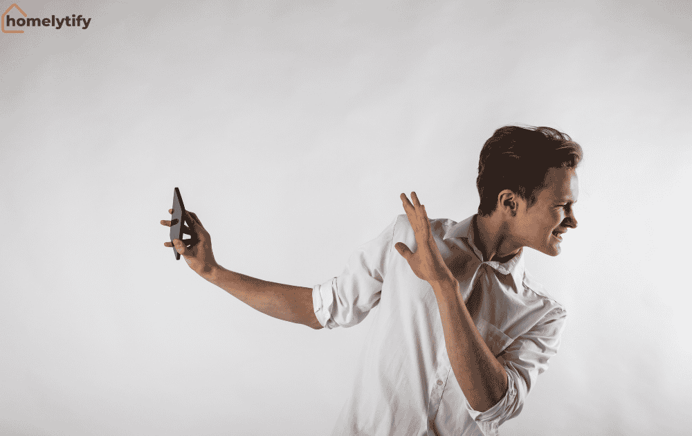Man avoiding his phone by pushing it away with a dismissive gesture against a plain light background.
