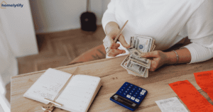 Woman counting cash at a wooden desk with a notebook and calculator while planning budget home tips.