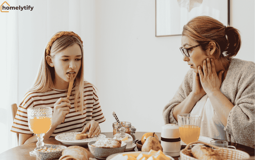 Mother and daughter eating something simple together at a breakfast table with bread, pastries, and orange juice.