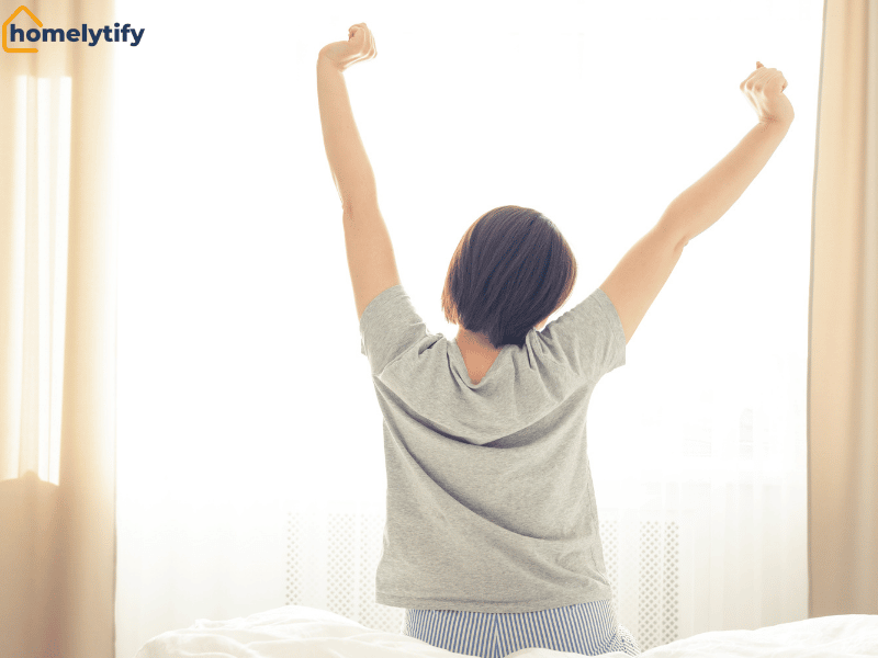 A woman stretching her arms in bed after waking up — a simple way to handle your body before your schedule begins