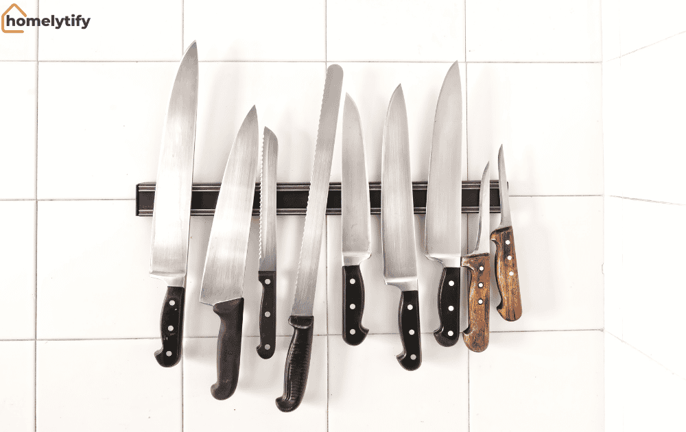 Magnetic knife strip on the wall holding multiple kitchen knives neatly against white tiles for safe and space-saving storage.