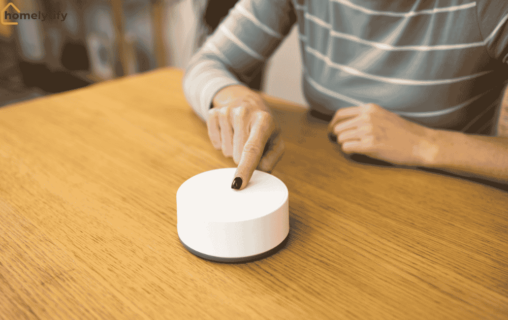 A woman pressing a white smart hub device placed on a wooden table at home.