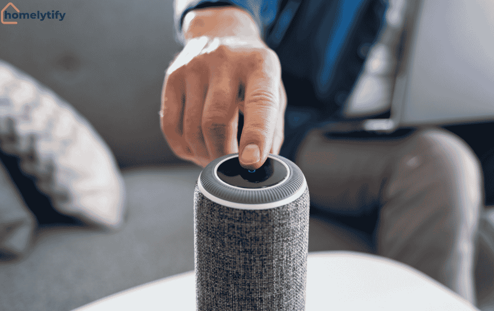 A man tapping the top button of a smart speaker and voice assistant placed on a white table in a living room
