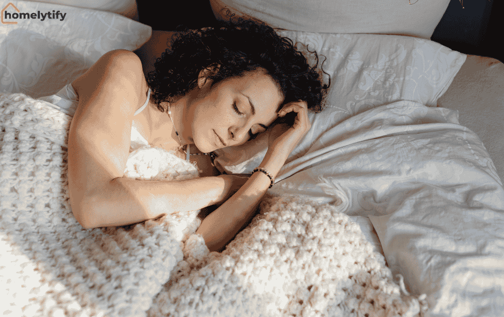 Woman sleeping soundly in bed with a knit blanket, night before tips for a better morning routine.