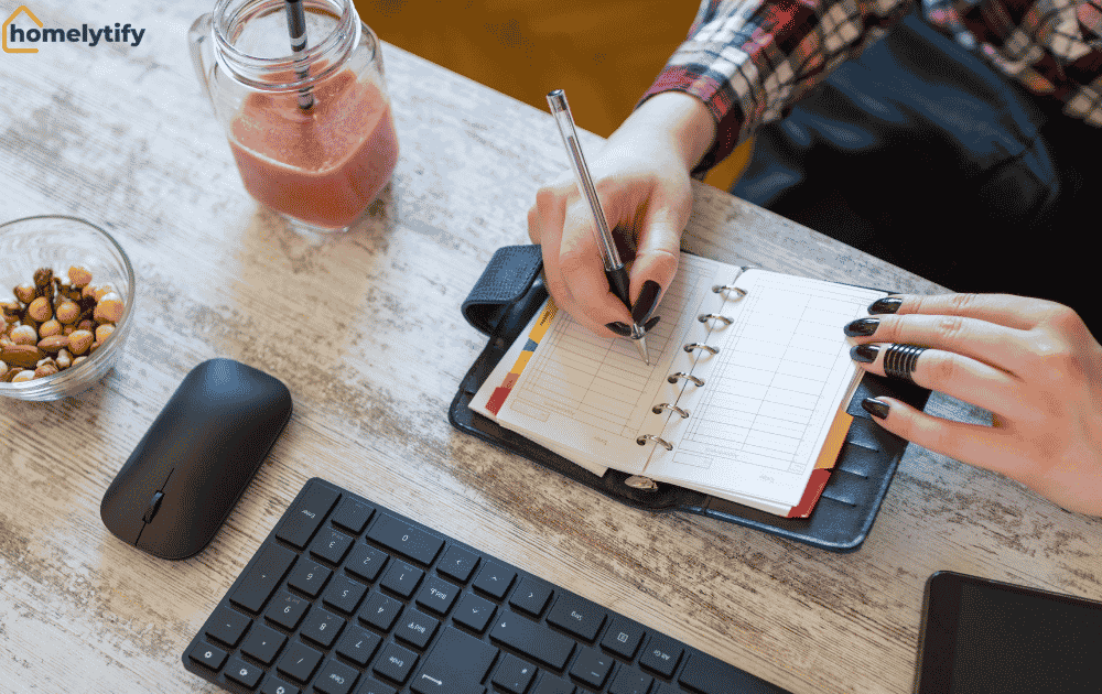 Woman writing down her three most important tasks in a planner on a desk with a keyboard, mouse, and smoothie.