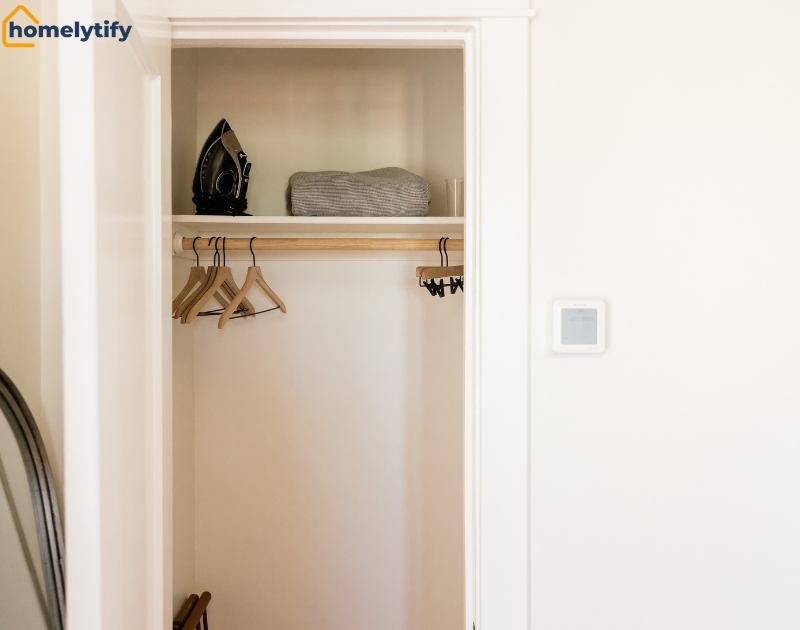 Clean back of the closet door space with wooden hangers, top shelf holding an iron and folded towels.