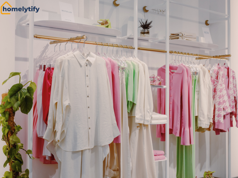 A way to double your hanging space using two parallel gold rods holding pastel shirts and tops in a bright white closet display 