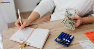 Person writing notes and counting cash with a calculator showing how to reduce household expenses on a budget 