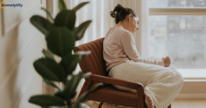 A woman practicing relaxing evening habits by journaling quietly in a cozy armchair by the window with an indoor plant nearby 