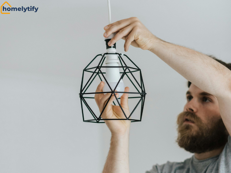 Man screwing in the bulb into a geometric wire pendant light fixture.