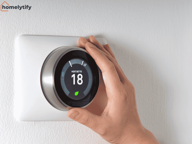 A hand adjusting a smart thermostat set to 18 degrees on a white wall for energy-efficient home temperature control 