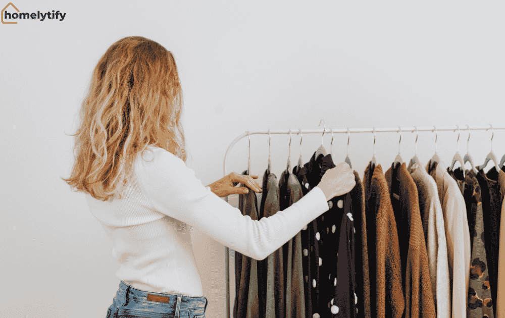 A woman browsing through clothes on an open rack — start with a clothing audit, not a shopping trip, to better organise your small space.