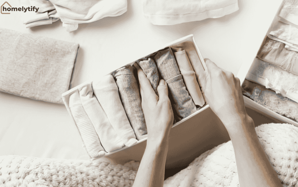 Hands neatly arranging rolled clothes into storage boxes using the fold and stack method for compact, small room organisation.