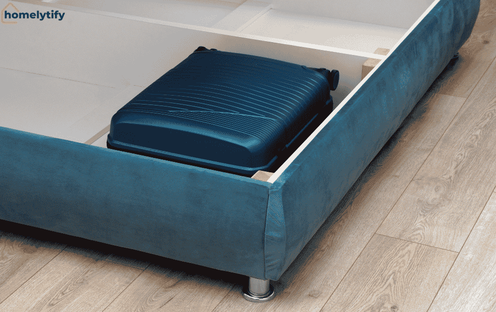 A suitcase tucked beneath a blue bed frame shows how under-bed storage maximises space in a small room.