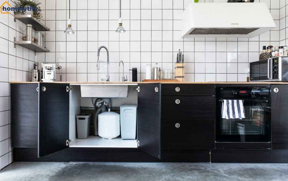 Open black cabinet doors showing the space under your kitchen sink with a trash bin, water filter, and pipes organized neatly